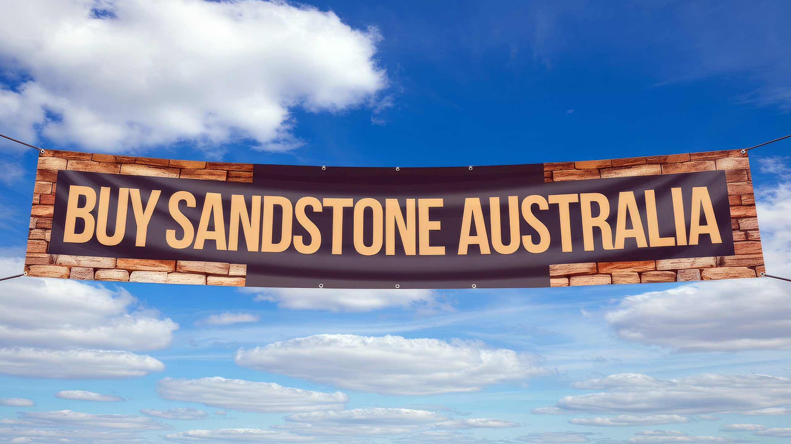 A banner with the words "BUY SANDSTONE AUSTRALIA" in bold letters, set against a blue sky with scattered white clouds. The banner appears to be held up by ropes at its sides.