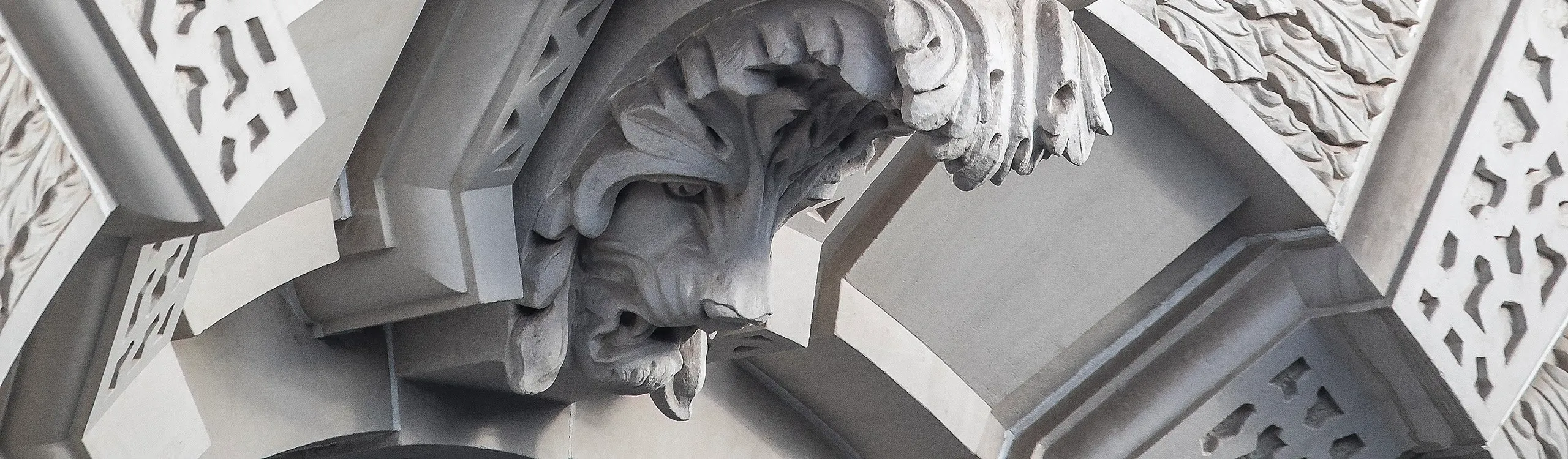 Ornate stone architectural detail featuring a carved lion head under an archway, showcasing intricate artistry and craftsmanship. The surrounding stonework includes decorative patterns that enhance the overall aesthetic.